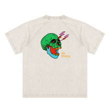 Load image into Gallery viewer, A light beige short-sleeve raglan t-shirt featuring a colorful graphic of a green skull with yellow teeth, lightning bolts, and a blue dotted pattern on the chest, with 'Pop America' text printed below.